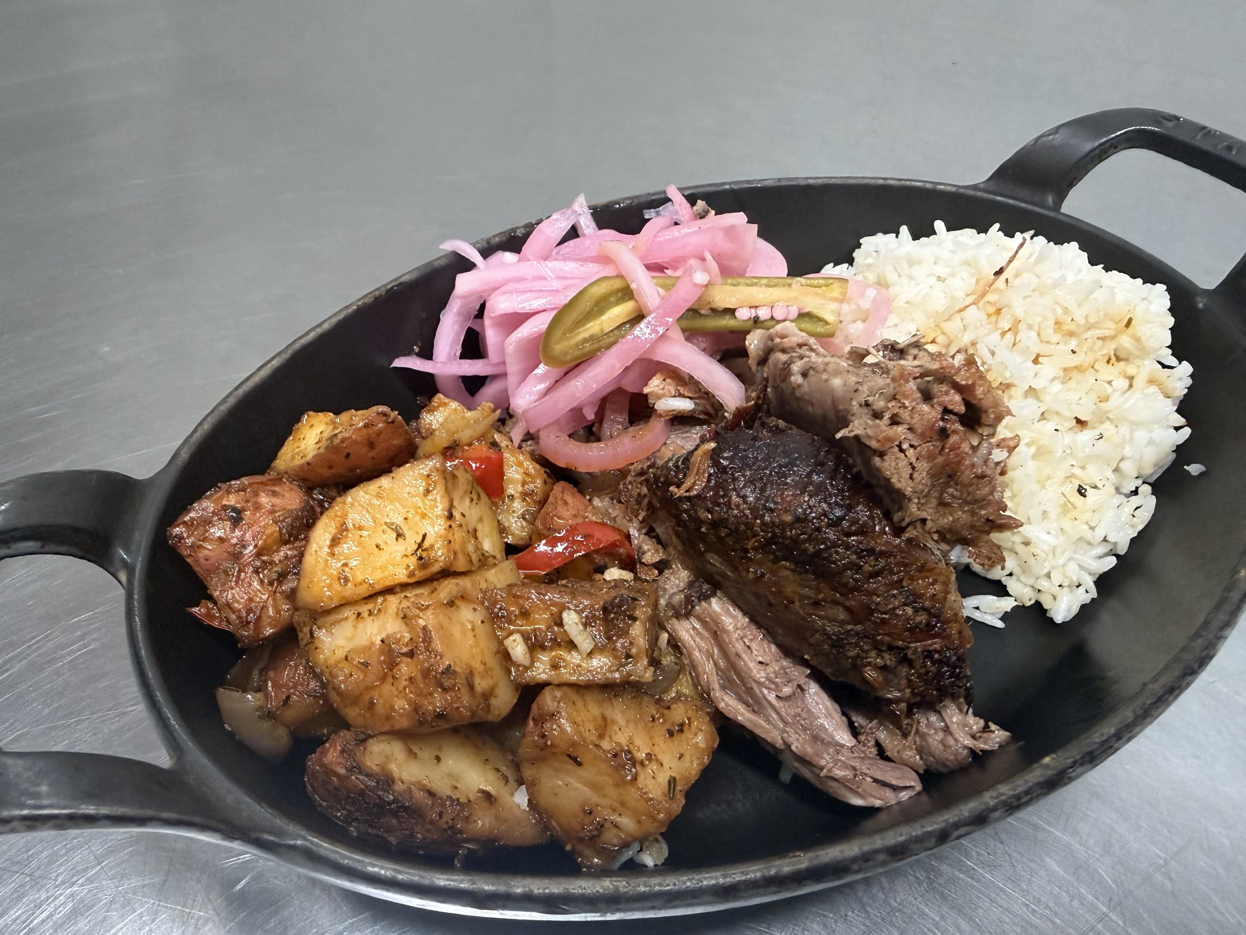 A close-up of a sizzling platter featuring tender roasted meat, seasoned potatoes, pickled onions, and fluffy white rice, showcasing a colorful and flavorful dish perfect for a hearty meal.