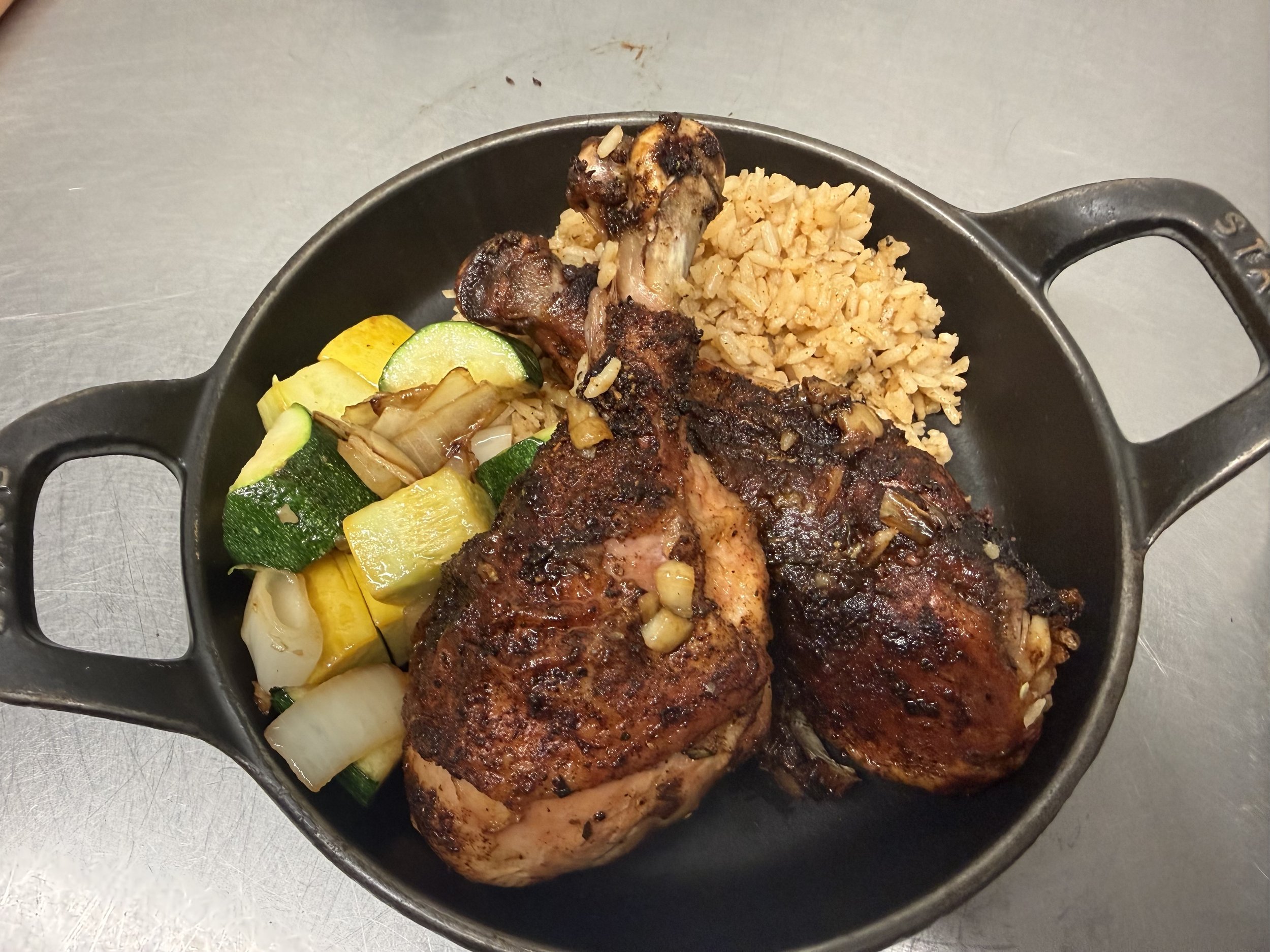 Deliciously seasoned roasted chicken thighs served with a side of fluffy rice and sautéed zucchini, yellow squash, and onions in a cast-iron skillet. Perfect for a hearty meal.