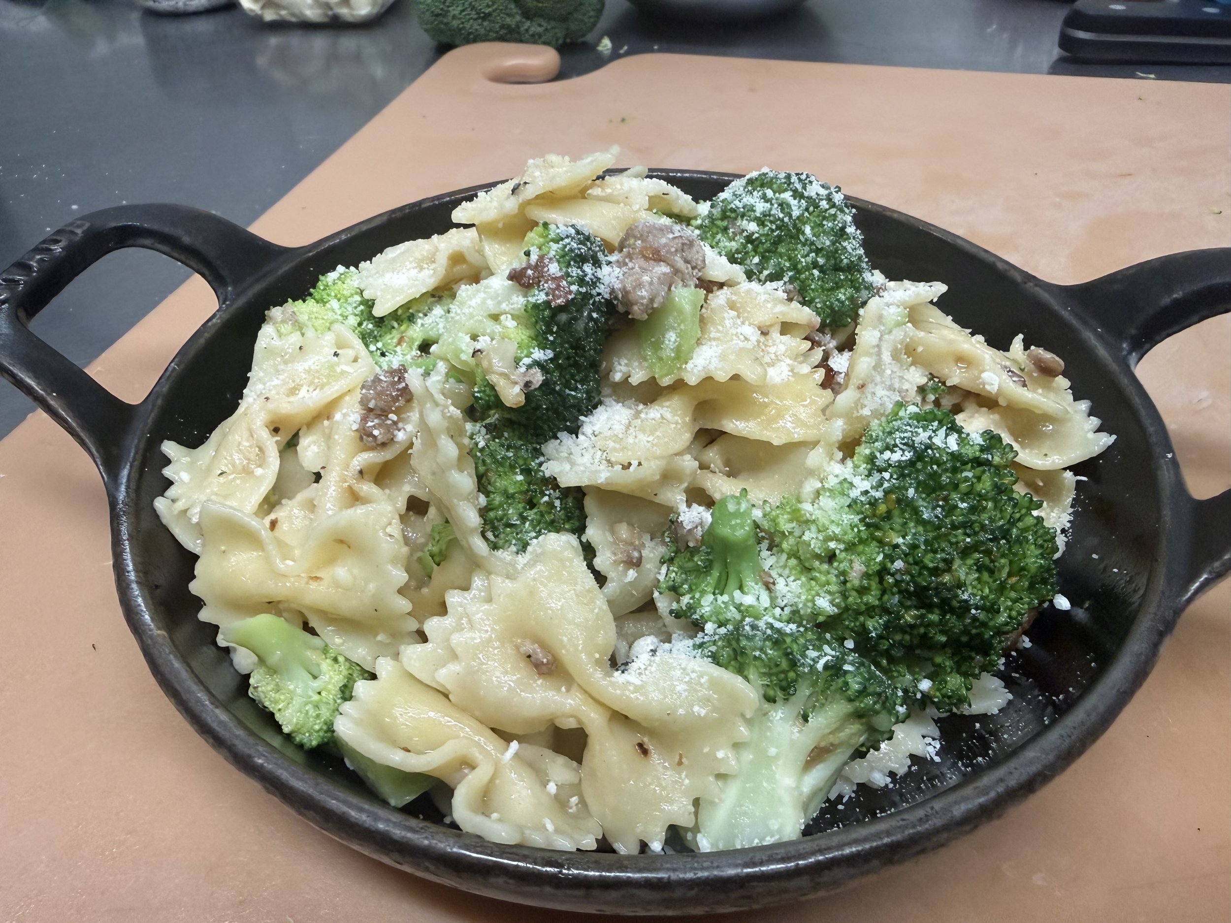A cast iron skillet filled with farfalle pasta tossed with broccoli, ground meat, and topped with grated cheese, set on a kitchen countertop.