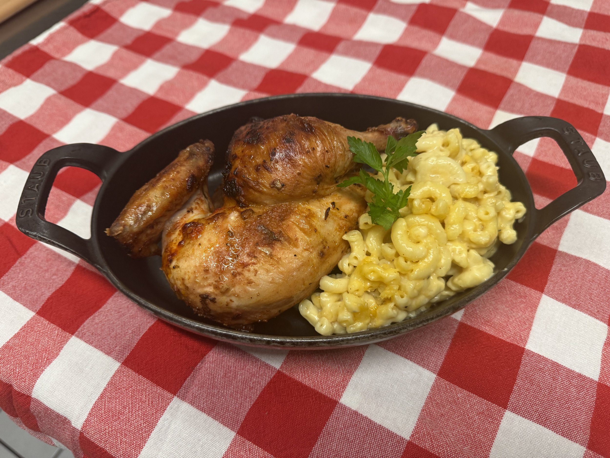 Delicious roasted chicken served with creamy macaroni and cheese in a black cast iron skillet, set on a red and white checkered tablecloth.