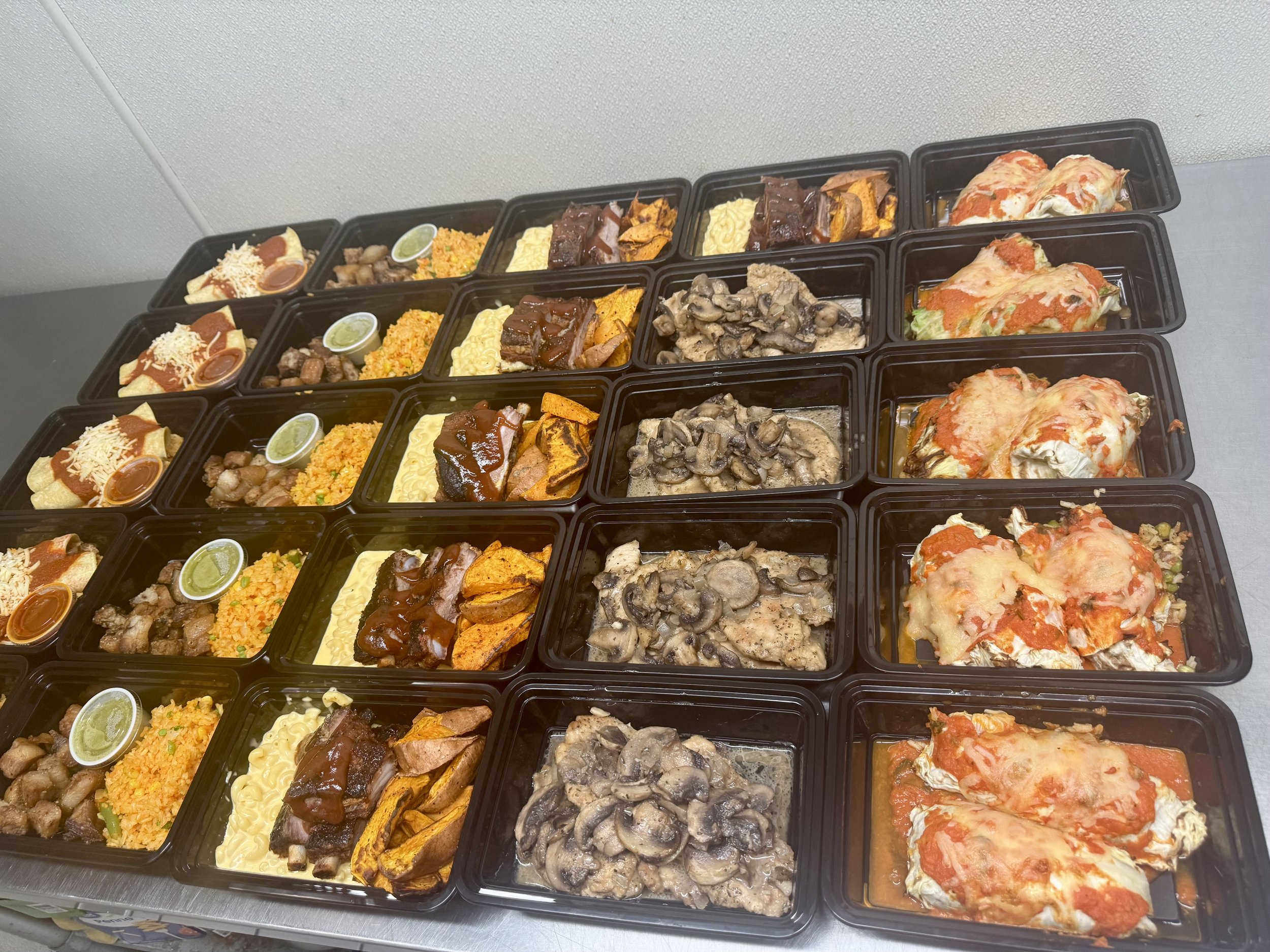 Assorted meal prep containers featuring a variety of dishes including grilled meats, rice, pasta, roasted sweet potatoes, and enchiladas, arranged neatly for meal planning.